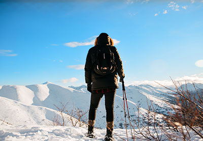 man in snow with coat and backpack, ski poles facing snow covered mountains
