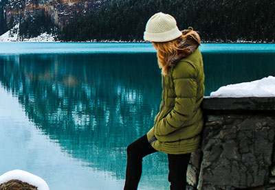 woman standing by snowy lake with coat and hat